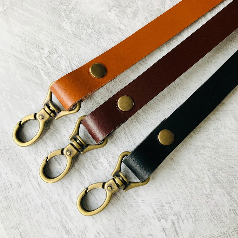 Three leather bag straps, black, brown and tan with antique brass lobster clasps and rivet detail