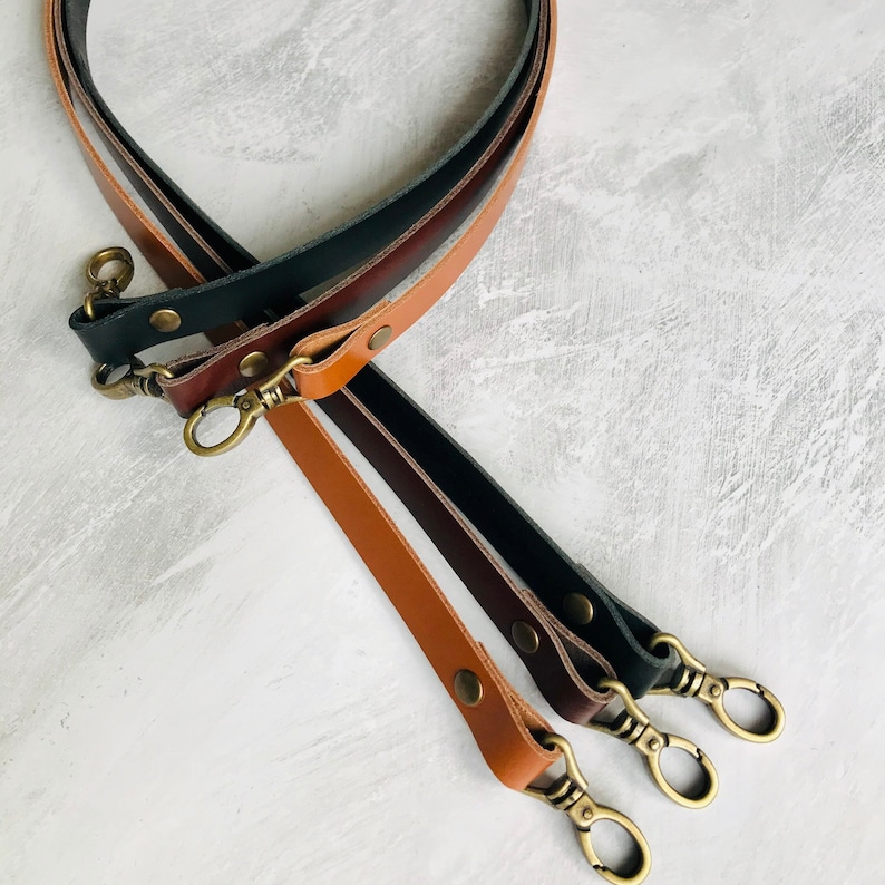 Three leather bag straps, black, brown and tan with antique brass lobster clasps and rivet detail