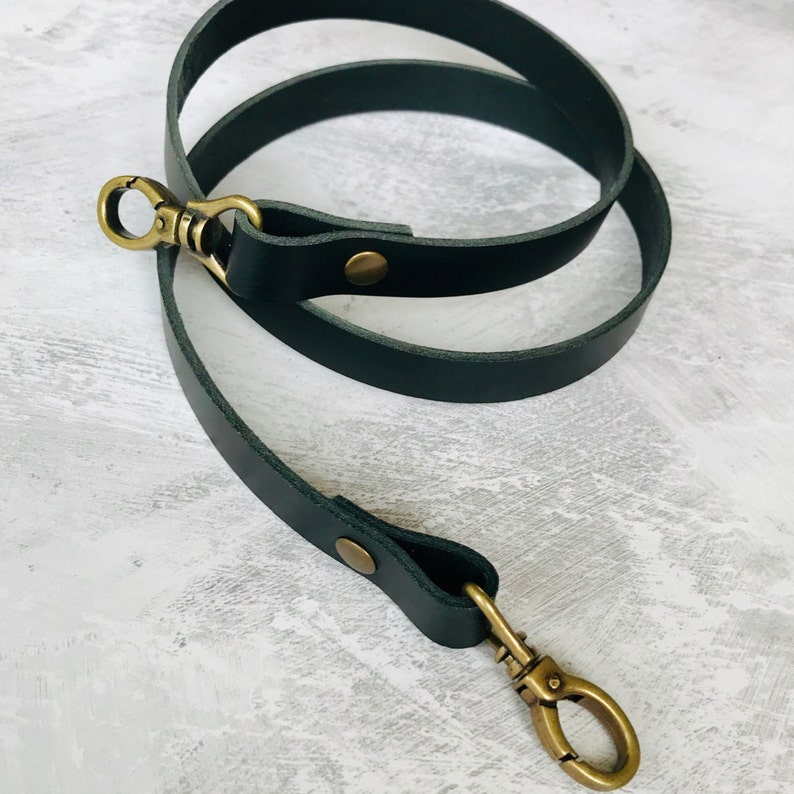 Black leather bag strap with an antique brass lobster clasp and rivet detail