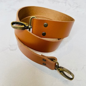May include: A brown leather strap with two brass swivel clasps. The strap is folded in half and the clasps are visible.
