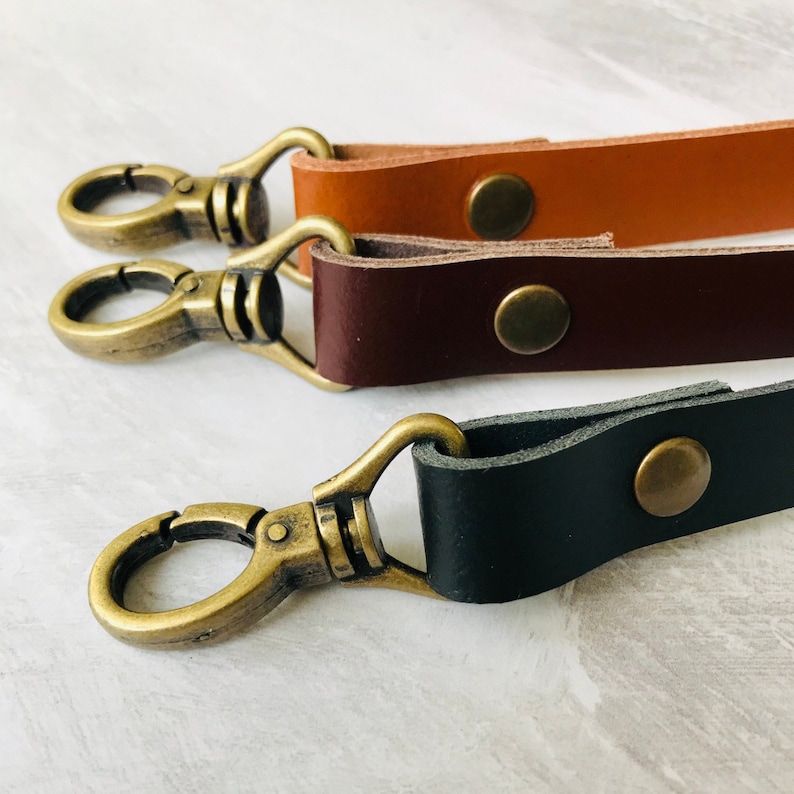 Three leather bag straps, black, brown and tan with antique brass lobster clasps and rivet detail