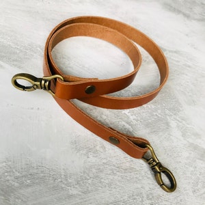 Tan leather bag strap with an antique brass lobster clasp and rivet detail