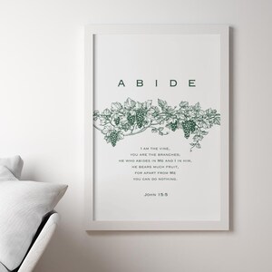 May include: A white framed print with a green vine and grapes illustration. The print has the word "ABIDE" in large letters at the top and a Bible verse from John 15:5 below the illustration.