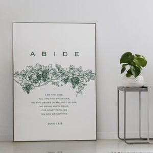May include: A framed print with a green vine and grapes design. The print has the word "ABIDE" in large letters at the top and a Bible verse from John 15:5 below the image. The verse reads: "I am the vine, you are the branches. He who abides in me and I in him, he bears much fruit. For apart from me you can do nothing. John 15:5."