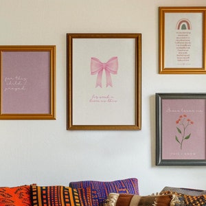 Puede incluir: Cuatro impresiones enmarcadas con fondos rosas y texto blanco cuelgan de una pared blanca. Las impresiones presentan un lazo rosa, un diseño floral y el texto "for this child I prayed" y "Jesus loves me this I know".