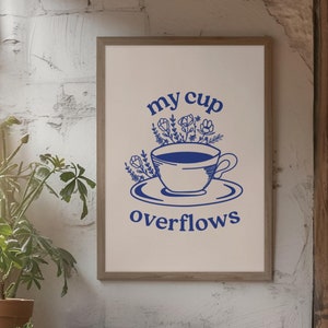May include: A white framed print with a blue illustration of a cup overflowing with flowers. The text "my cup overflows" is printed below the cup.