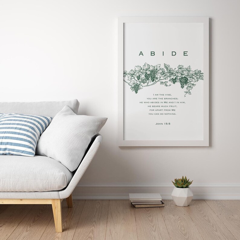 May include: A white framed print with a green vine and grapes illustration. The print has the word "ABIDE" in large letters at the top and a Bible verse from John 15:5 below the illustration.