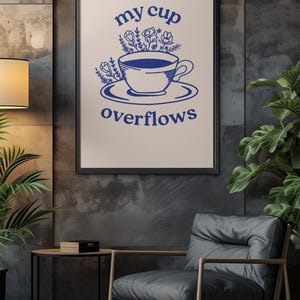 May include: A framed print with a blue illustration of a cup overflowing with flowers. The text "my cup overflows" is written below the cup.