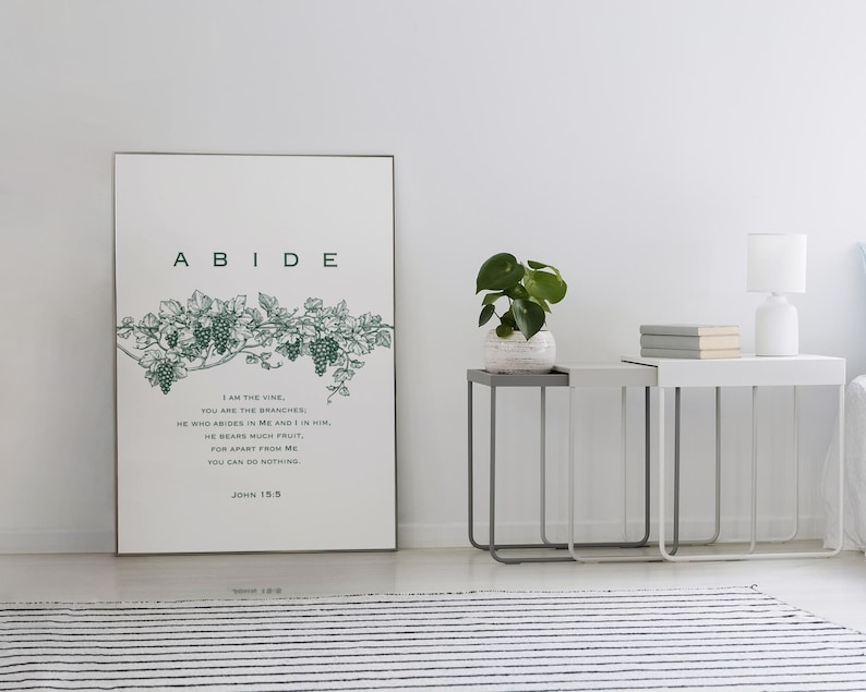 May include: A framed print with a green vine and grapes design. The print has the word "ABIDE" in large letters at the top and a Bible verse from John 15:5 below the image. The verse reads: "I am the vine, you are the branches. He who abides in me and I in him, he bears much fruit. For apart from me you can do nothing. John 15:5."