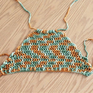 May include: A crocheted top with a scalloped edge in shades of green and orange. The top has long ties that can be adjusted for a custom fit.