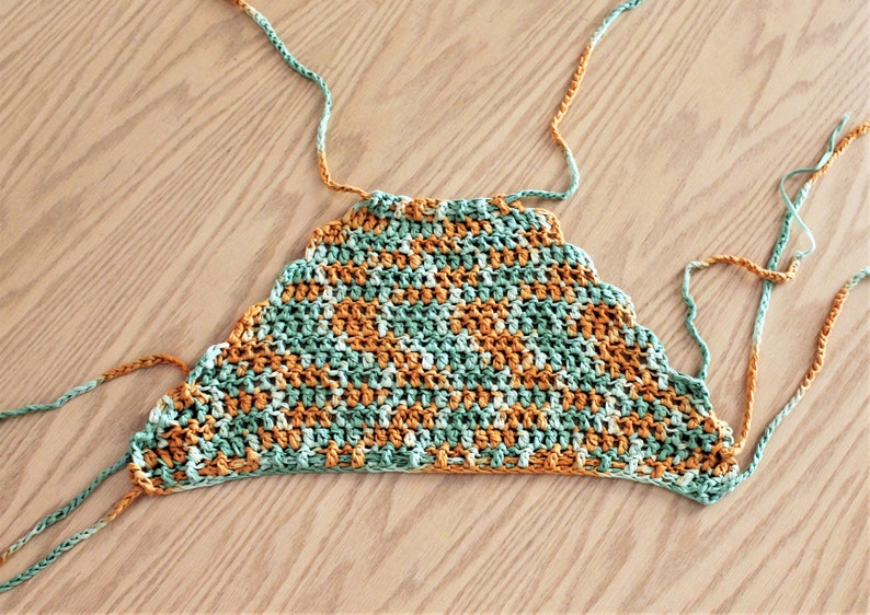 May include: A crocheted top with a scalloped edge in shades of green and orange. The top has long ties that can be adjusted for a custom fit.