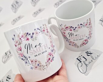 May include: Two white ceramic mugs with floral designs and the text "Mrs. Smith 06.07.2024" and "Mr. Smith 06.07.2024" printed on them.