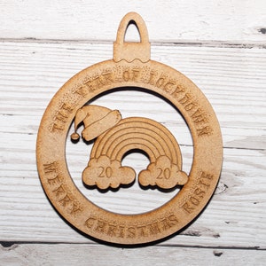 May include: A wooden Christmas ornament with a rainbow and a Santa hat inside a circle. The text around the circle reads "The Year of Lockdown Merry Christmas 2020 Rosie".