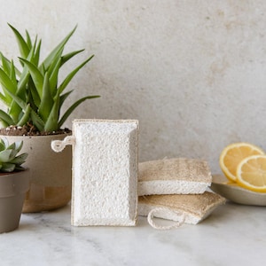 May include: Three white loofah sponges with a natural jute backing. The sponges are stacked on top of each other and have a white string attached to the top sponge.