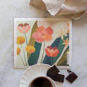 May include: A white dishcloth with a floral design featuring pink, orange, and yellow flowers on a green background. The text "EARTH AHEAD" is printed on the bottom right corner of the dishcloth.