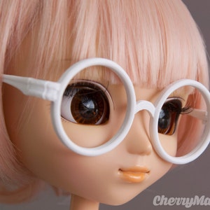 May include: A doll with pink hair wearing white round glasses.