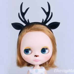 May include: A black deer antler headband with a black velvet band. The headband is worn by a doll with blonde hair and blue eyes.