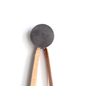 Puede incluir: Una correa de cuero marrón cuelga de un gancho redondo de metal gris oscuro.