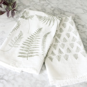 Fern Fronds Tea Towel Set of 2 for the kitchen. One white flour sack tea towel is covered by a variety of large sage green fern fronds and the other white towel is covered by a pattern of small repeating sage green fern leaves.