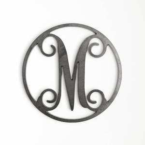 May include: A black metal monogram letter M in a circular frame. The letter is stylized with decorative flourishes.