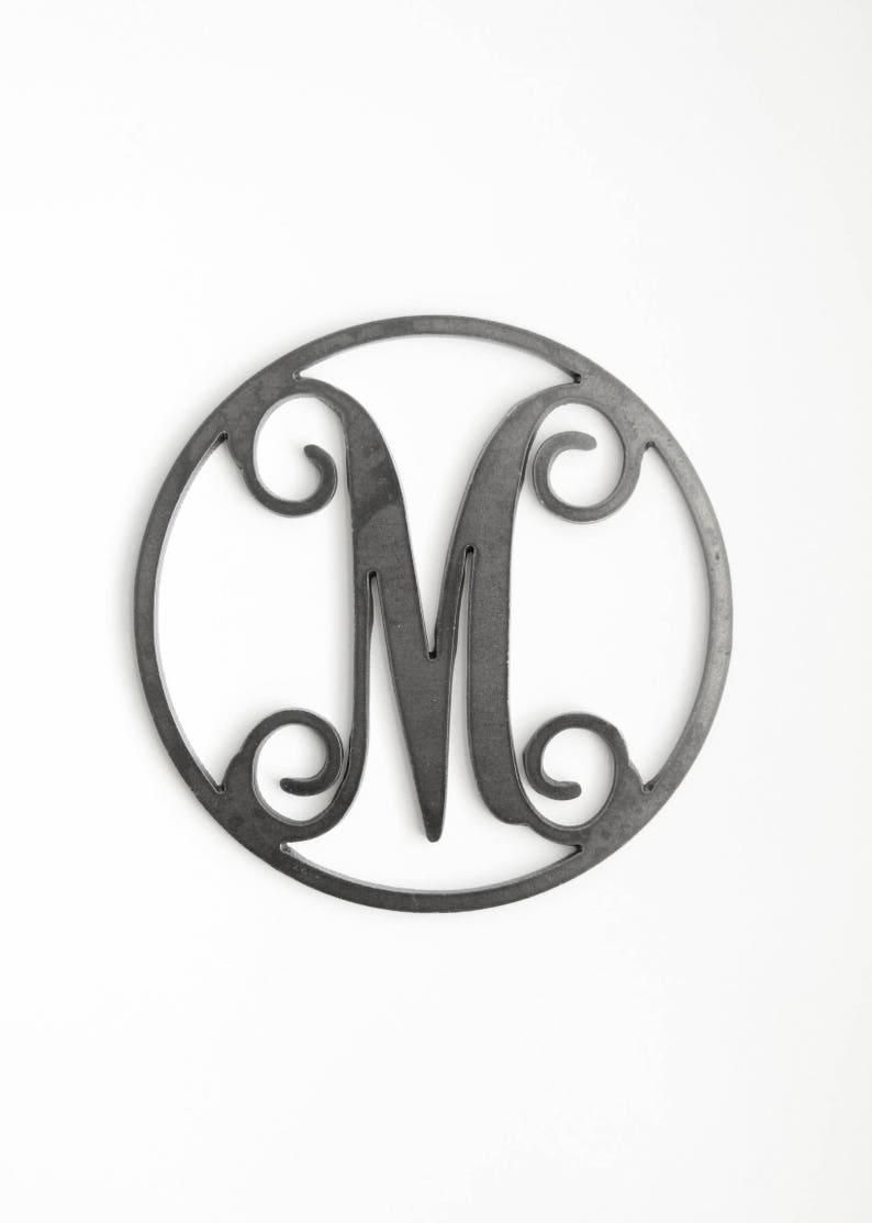 May include: A black metal monogram letter M in a circular frame. The letter is stylized with decorative flourishes.