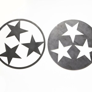 Puede incluir: Dos piezas de arte mural circulares de metal con un dise&ntilde;o de estrellas recortadas. La pieza de la izquierda es un marco circular fino con tres estrellas de metal s&oacute;lido en su interior. La pieza de la derecha es un disco de metal s&oacute;lido con tres recortes en forma de estrella.