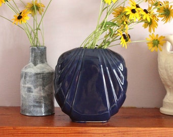 May include: Two ceramic vases with yellow flowers. The vase on the left is gray and textured. The vase on the right is blue and has a scalloped design.