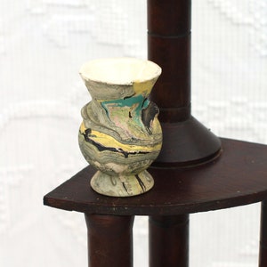 May include: A wooden tiered stand with three levels, each with a circular top. The stand is dark brown and has a decorative design. A small, white, and multi-colored ceramic vase sits on the top level.