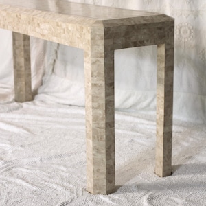 May include: A rectangular console table with a mosaic tile design in shades of beige and grey. The table has four sturdy, rectangular legs and a smooth, polished surface. The table is approximately 122 cm long, 41 cm wide, and 76 cm high.
