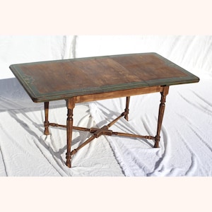 May include: A wooden table with a green painted border around the top. The table has a cross-shaped base and four legs.