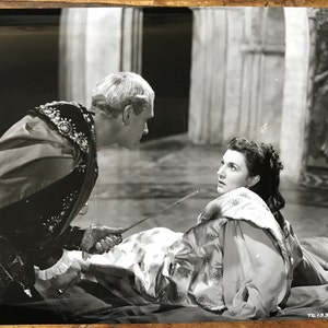 Könnte beinhalten: Ein Schwarzweißfoto einer Szene aus einem Theaterstück. Ein Mann in einem dunklen Gewand hält ein Schwert über einer Frau, die auf dem Boden liegt.