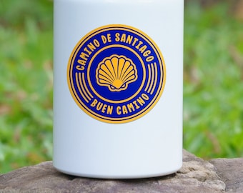 May include: White water bottle with a blue and gold sticker that says "Camino de Santiago Buen Camino" and features a scallop shell.