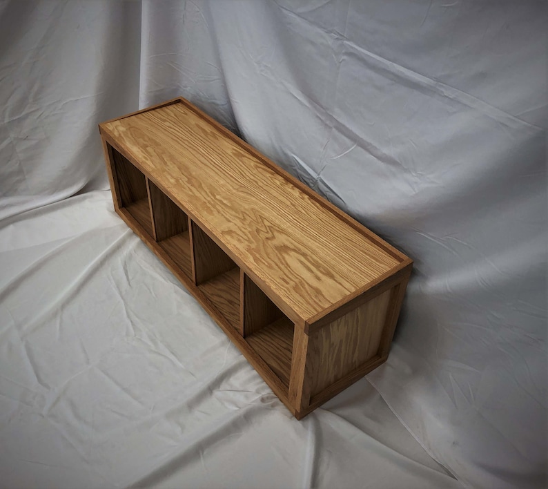 May include: A wooden shelf unit with four compartments. The shelf is made of light brown wood with a natural grain pattern. The shelf is mounted on a wall.