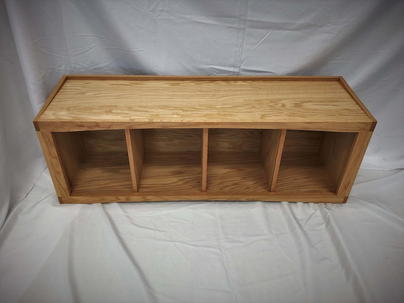 May include: A wooden shelf unit with four open compartments. The shelf is made of light brown wood with a natural finish.