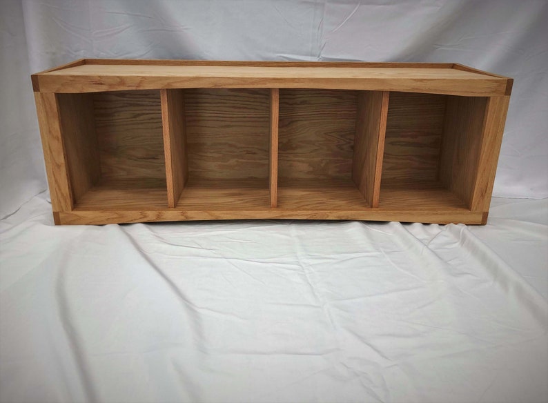 May include: A wooden shelf unit with four open compartments. The shelf is made of light brown wood with a natural finish.