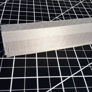 Puede incluir: Primer plano de un pequeño objeto gris impreso en 3D. El objeto tiene forma rectangular y una superficie ligeramente curvada. Parece ser una pequeña pieza o componente.