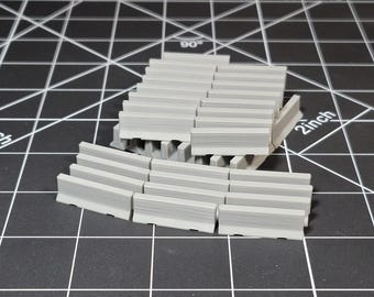 May include: A set of 18 grey concrete barriers, some curved and some straight, arranged in a semi-circle on a black grid surface. The barriers are approximately 5 cm long.