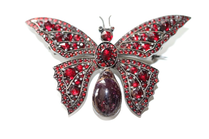 May include: A silver butterfly brooch with red gemstone accents. The brooch features a large, teardrop-shaped gemstone in the center.