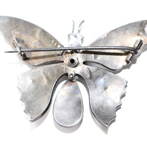 May include: Silver butterfly brooch with a pin on the back. The butterfly has a detailed design and a teardrop-shaped body.