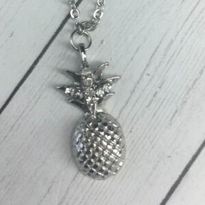 May include: A silver pineapple necklace with a chain and clear rhinestones on the top of the pineapple.