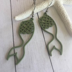 May include: A pair of green mermaid tail earrings with a silver hook. The earrings are made of a lightweight material and have a delicate design.