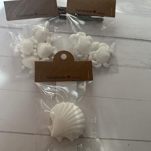May include: Three bags of white ceramic sea life decorations. The bags are clear plastic with brown paper tags that say "Handmade with Love". The decorations include a seashell, crabs, and sea turtles.