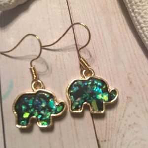 May include: A pair of gold elephant earrings with green iridescent glitter inside.