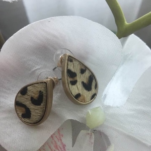 May include: A pair of gold tone teardrop shaped earrings with a leopard print design. The earrings are made of faux fur and have a gold tone post.
