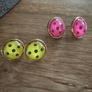 May include: A pair of earrings with a polka dot design. One pair is pink with black dots and the other pair is yellow with black dots.