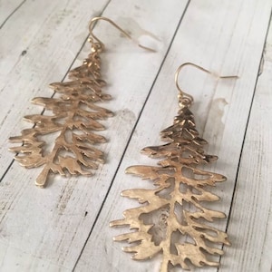 May include: A pair of gold-tone earrings shaped like pine trees. The earrings are delicate and have a cutout design.