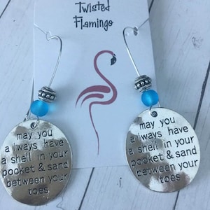May include: Silver dangle earrings with blue glass beads and a silver charm with the text "may you always have a shell in your pocket & sand between your toes".