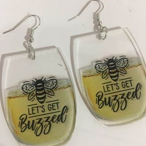 May include: A pair of clear acrylic earrings shaped like wine glasses with a bee and the text "Let's Get Buzzed".