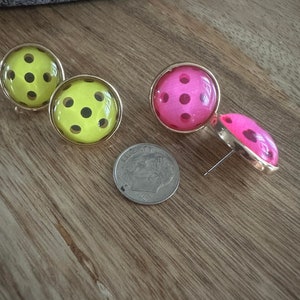 May include: A pair of earrings with a polka dot design. One pair is yellow with black dots and the other pair is pink with black dots.
