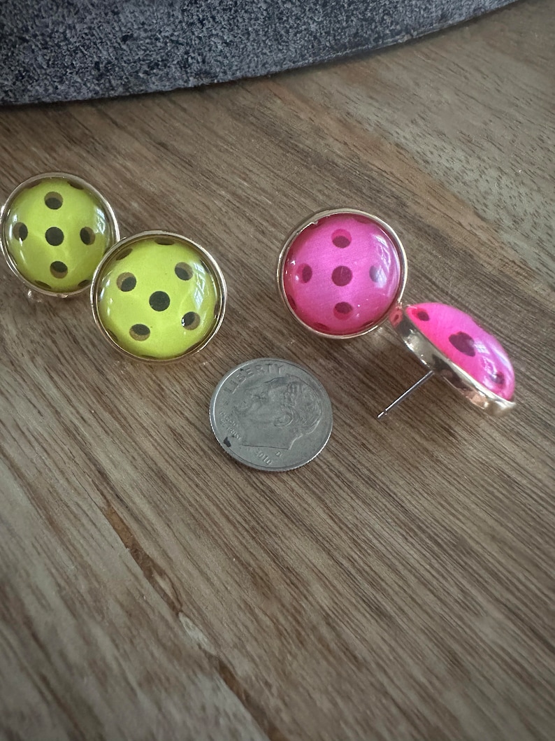 May include: A pair of earrings with a polka dot design. One pair is yellow with black dots and the other pair is pink with black dots.